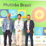 Tr&ecirc;s homens adultos est&atilde;o em p&eacute;, lado a lado, posando para uma foto em um ambiente interno. Eles vestem roupas sociais &mdash; blazers, camisas e cal&ccedil;as &mdash; e usam crach&aacute;s pendurados no pesco&ccedil;o. Todos est&atilde;o olhando para a c&acirc;mera, com express&otilde;es neutras a levemente sorridentes.

Ao fundo, h&aacute; um painel colorido com o t&iacute;tulo &ldquo;Mutir&atilde;o Brasil&rdquo; em destaque. O painel &eacute; composto por blocos com ilustra&ccedil;&otilde;es que remetem &agrave; sustentabilidade, como planeta Terra, s&iacute;mbolo de reciclagem, folhas e gr&aacute;ficos. Na parte superior, aparecem logotipos de organiza&ccedil;&otilde;es como C40 Cities, Global Covenant of Mayors for Climate & Energy e FNP.

O ch&atilde;o &eacute; claro e o ambiente &eacute; bem iluminado, com aspecto de evento institucional ou confer&ecirc;ncia.